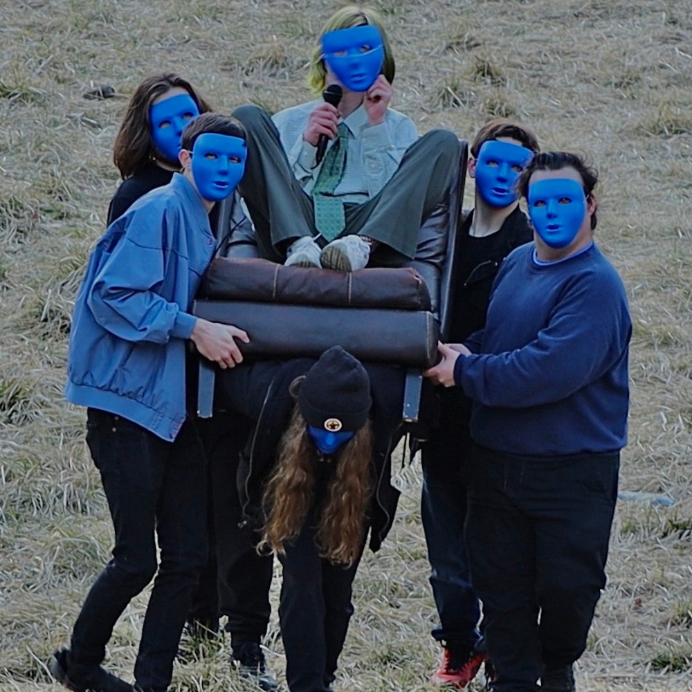 Bobby Nair in a chair being carries in seers with blue masks